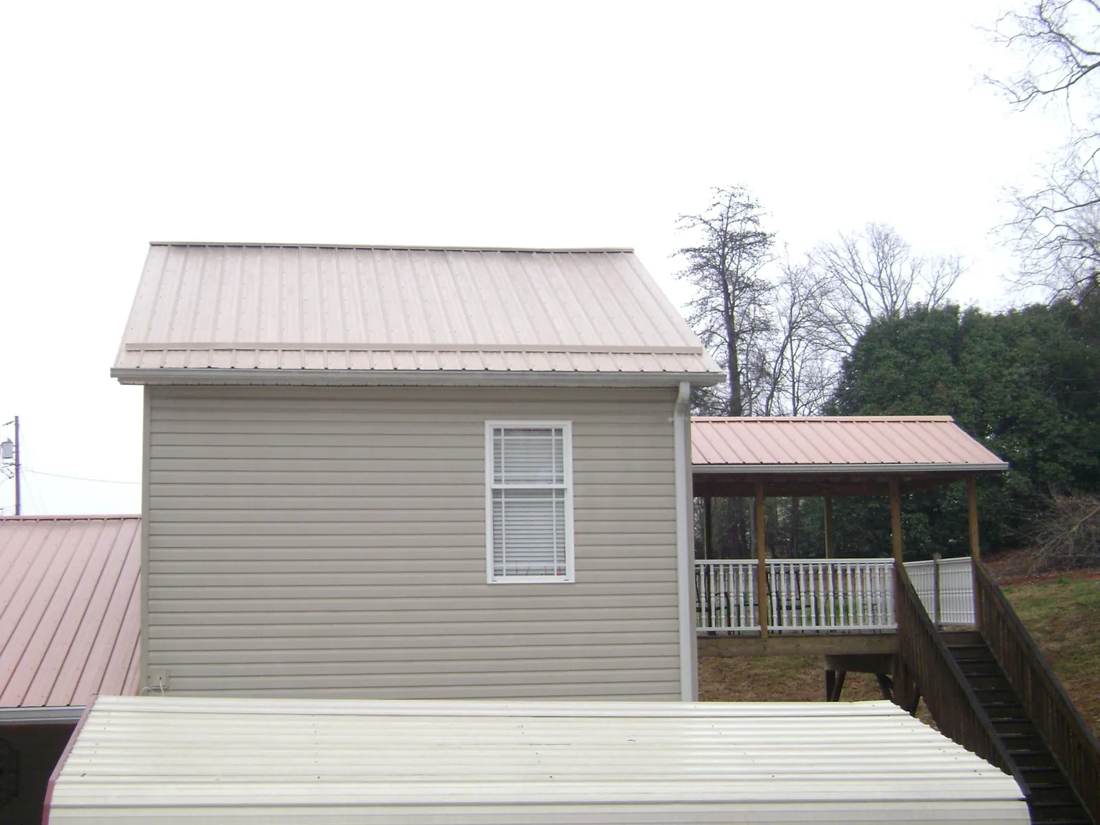 Tan metal roofs on a two story addition and attached porch, from a Roof Replacement job in Avoca